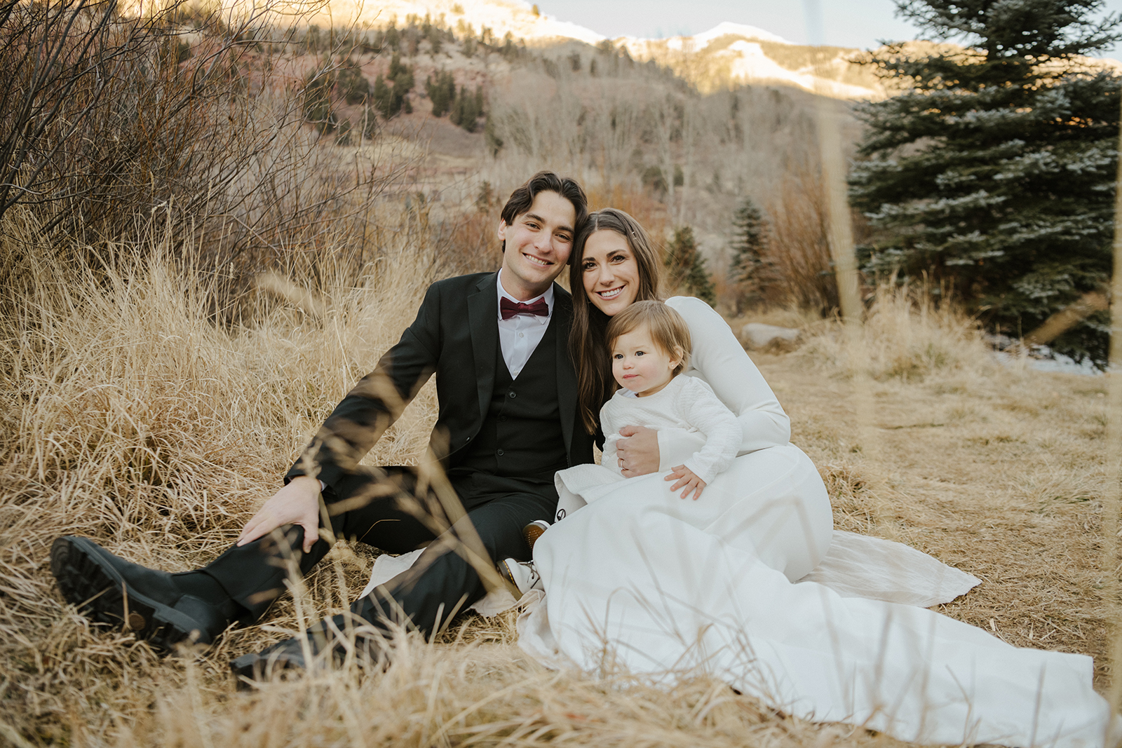 Family in wedding attire sitting on dried grass in the winter in Telluride
